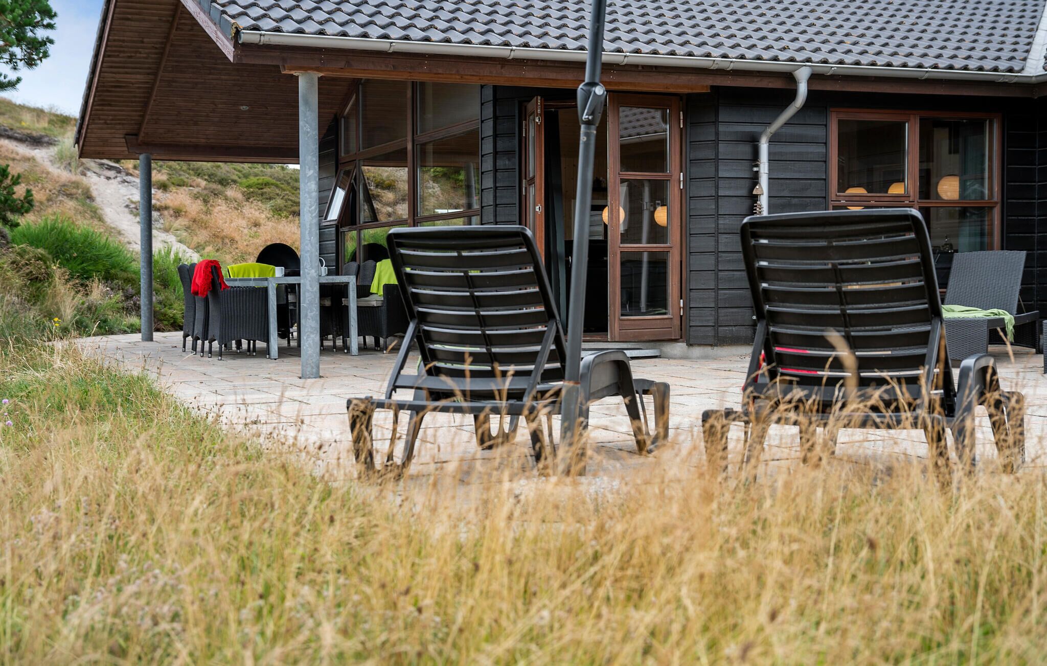 A building with a tiled roof, large windows, and outdoor seating with chairs.
