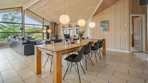 Une cuisine spacieuse avec une table et des chaises en bois, de grandes fenêtres et une vue sur l’extérieur.
