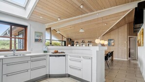 Une cuisine moderne dotée d’un îlot central, d’un plafond en bois et de grandes fenêtres.