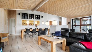 Un salon moderne avec un plafond en bois, un coin repas avec des chaises noires, un canapé en cuir noir et une table basse en bois.