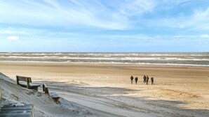 Une plage avec un rivage sablonneux, une promenade en bois et un groupe de personnes qui se promènent.