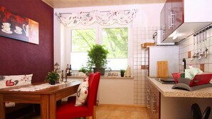 Une cuisine compacte avec un coin repas, comprenant une table en bois, des chaises rouges, une plante en pot et une fenêtre donnant sur un paysage verdoyant.
