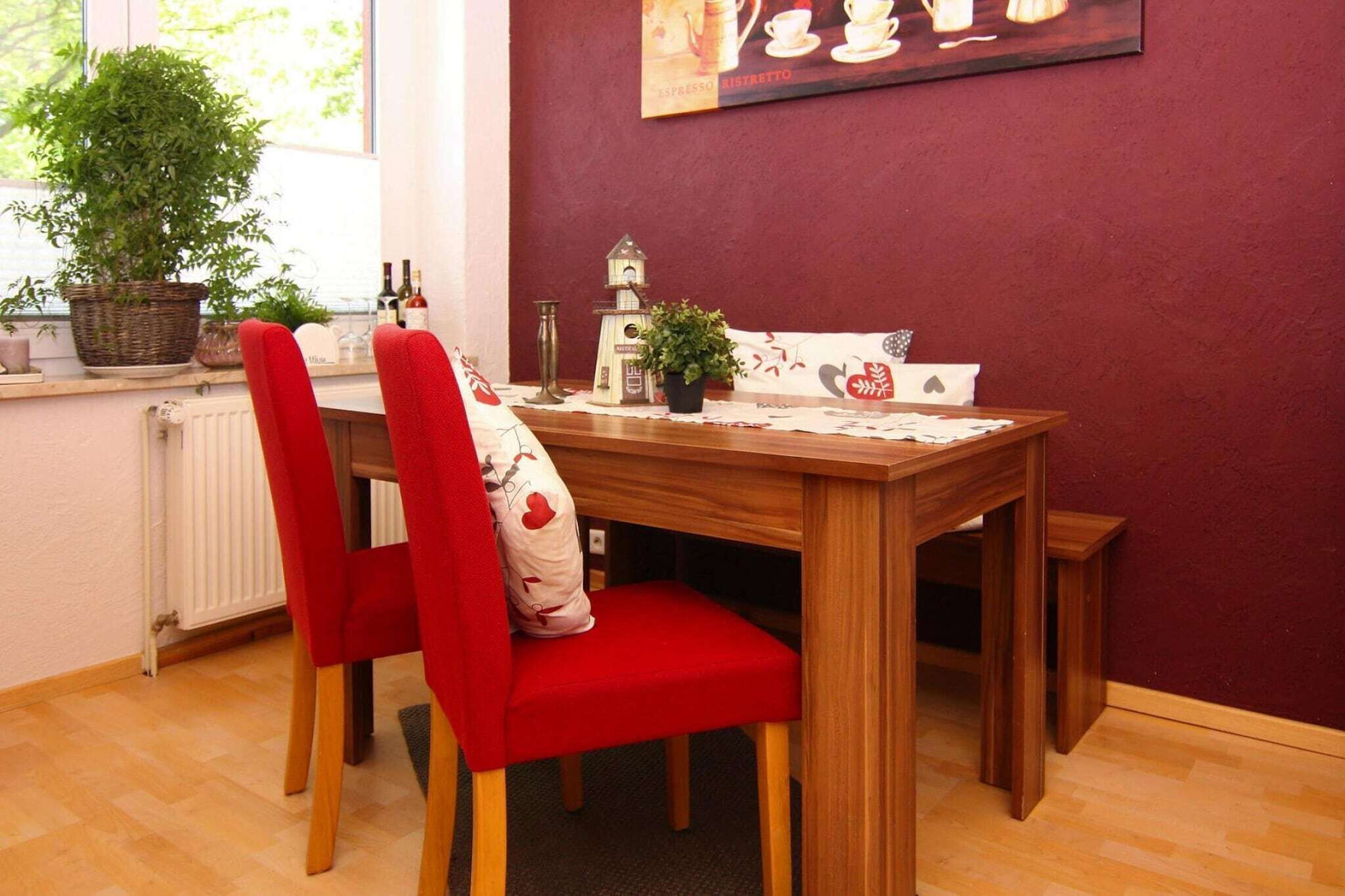 Ein Essbereich mit Holztisch, roten Sitzmöglichkeiten, einem Topfpflanzen, einer kleinen Glocke und einem gerahmten Bild an der Wand.