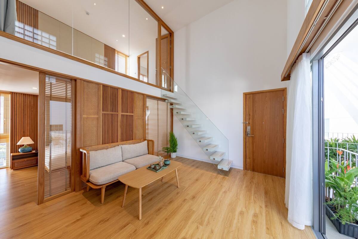A spacious living area with a wooden floor, a sofa, a coffee table, and a staircase leading to an upper level.