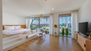 A modern hotel room with a large bed, a sofa, a TV, and a balcony with a view of the city.