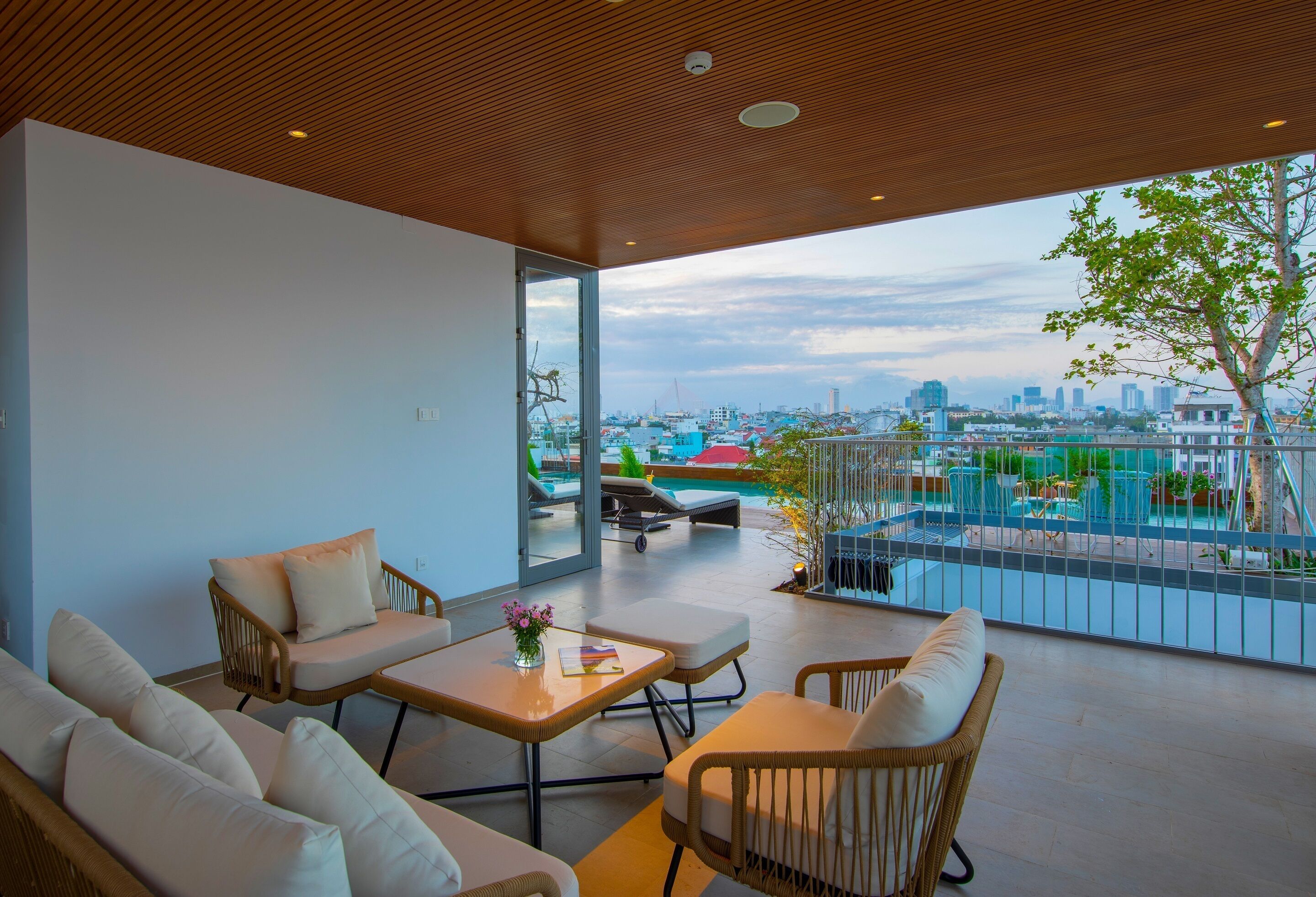 A modern living room with a city view, featuring a sofa, armchairs, a coffee table, and a balcony with a pool.