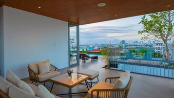 A modern living room with a city view, featuring a sofa, armchairs, a coffee table, and a balcony with a pool.