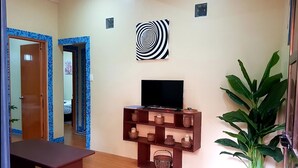 Ein Zimmer mit einem HolztV-Schrank, einer großen Topfpflanze und einem an der Wand befestigten Kunstwerk.