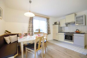 A compact kitchen with a dining area, wooden furniture, and a window with curtains. - Apartment in Flachau with Mountain Views (Flachau)