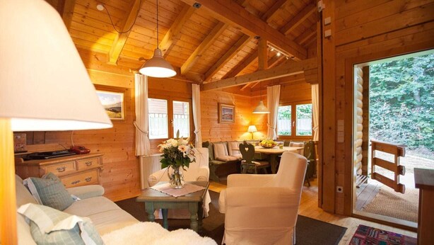 A cozy log cabin interior with a sofa, armchairs, a dining table, and a view of the forest. - Blockhäuser in Stamsried (Stamsried)