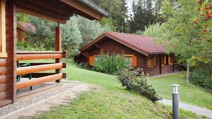 A wooden cabin with a red roof, surrounded by greenery and trees. - Blockhäuser in Stamsried (Stamsried)