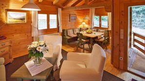 A wooden cabin interior with a dining area, a sofa, a table with a vase of flowers, and a window with a view of the outdoors. - Blockhäuser in Stamsried (Stamsried)