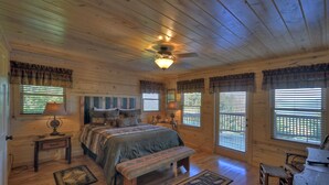 Quarto de cabana de madeira com uma cama, um banco e duas janelas com persianas.