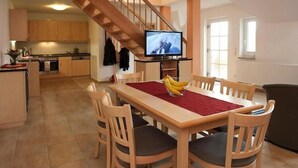 Eine moderne Küche mit Holzausbau, einem Essbereich mit rotem Tischläufer und einem Fernseher auf einem Schrank.
