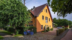 Ein gelbes Haus mit rotem Dach, Kopfsteinpflasterauffahrt und einem Fahrrad davor.