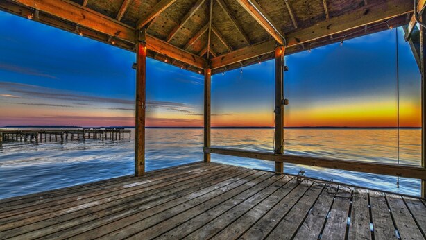 Una terraza de madera con vista al océano al atardecer.