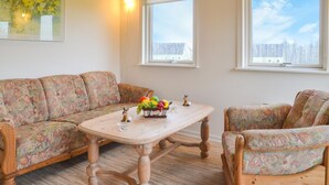 A living room with a floral-patterned sofa, a wooden coffee table with fruit and a figurine, and two windows with a snowy view. - 1 bedroom cozy home in Grindsted (Grindsted)