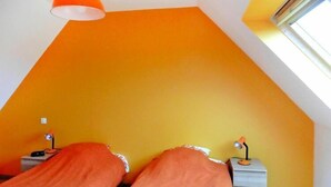 A room with a sloped ceiling and orange walls. There are two bedside tables with lamps. - Cottage in Brittany with Stunning Sea Views (Telgruc-sur-Mer)