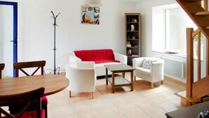 A living room with a white sofa, a red throw, a wooden coffee table, and a bookshelf. - Cottage in Brittany with Stunning Sea Views (Telgruc-sur-Mer)