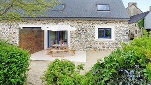 A stone house with a patio, a wooden door, and a small table with chairs. - Cottage in Brittany with Stunning Sea Views (Telgruc-sur-Mer)