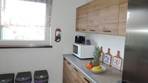 A kitchen with wooden cabinets, a microwave, a toaster, and a refrigerator. There are three trash bins and a window with a curtain.