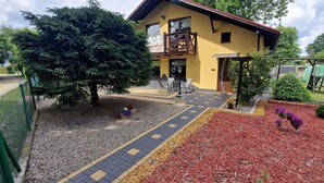 A yellow building with a balcony, a paved walkway, and a garden area with red mulch and gravel.