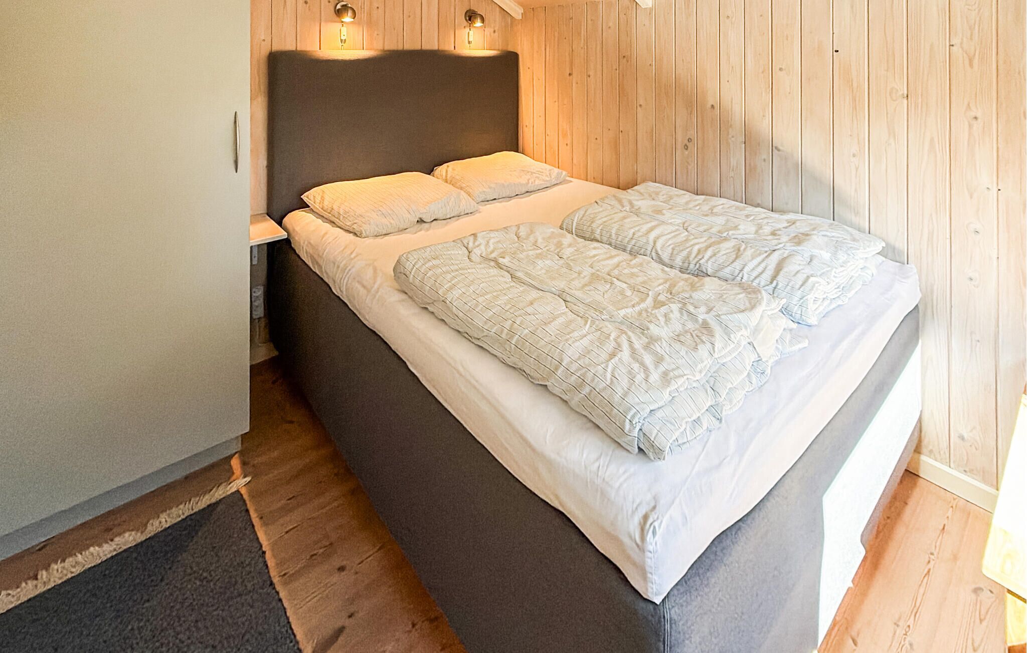 A bed with a headboard, two bedside lamps, and a wooden wall.