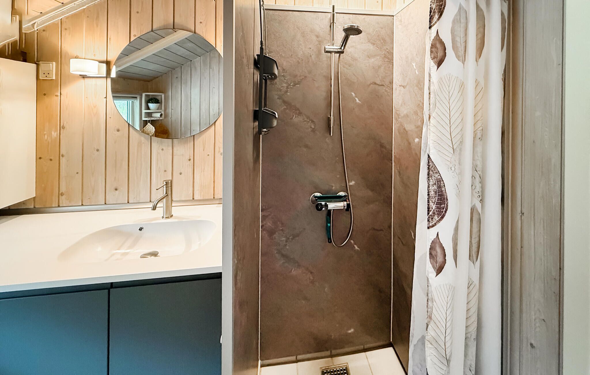 A bathroom with a wooden vanity, a sink, a mirror, and a shower enclosure.