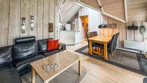 A modern living room with a black leather sofa, a wooden coffee table, and a dining area with a wooden table and chairs. - Beautiful home in Blåvand with WiFi (Blåvand)