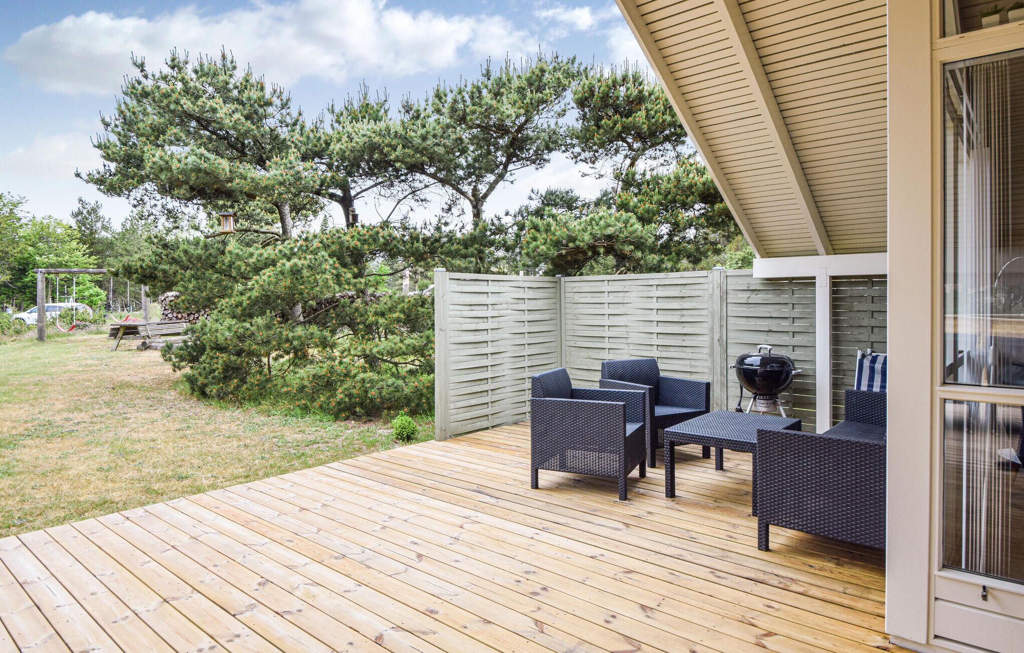 Een terras buiten met rieten meubels, een barbecue en een houten omheining.