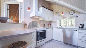 A modern kitchen with white cabinetry, a built-in oven, a stainless steel dishwasher, and a window providing natural light. - Beautiful home in Blåvand with WiFi (Blåvand)