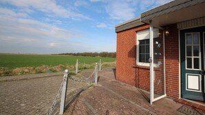 A brick building with a green door, a window, and a chain-link fence in front. - Holiday Bungalow in Dornumersiel (Dornumersiel)