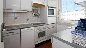 A compact kitchen with white cabinets, a built-in oven, a microwave, and a window with curtains. - Holiday Bungalow in Dornumersiel (Dornumersiel)