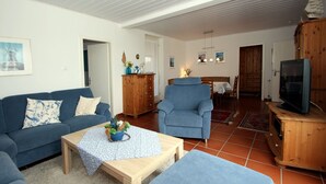 A living room with a blue sofa, a wooden coffee table, a blue armchair, and a television on a wooden cabinet. - Holiday Bungalow in Dornumersiel (Dornumersiel)