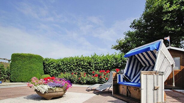 A lounge area with a planter of colorful flowers, a striped lounge chair, and a small structure with a blue awning. - Holiday Bungalow in Dornumersiel (Dornumersiel)