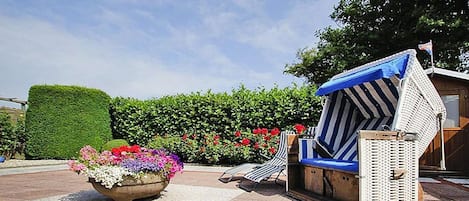 Un área de descanso con un macetero de flores coloridas, una silla lounge a rayas y una estructura pequeña con toldo azul.