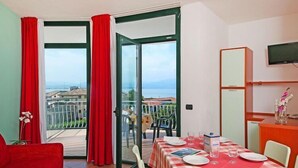 A room with a balcony, a dining table set with plates and glasses, and a television mounted on the wall.