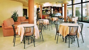 A hotel lobby with round tables, a sofa, and a bar area.