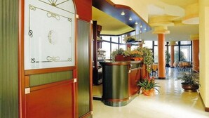 A hotel lobby with a reception desk, large windows, and a central plant arrangement.