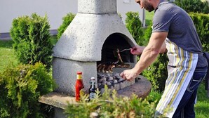A person grilling outdoors using a stone-built outdoor oven.