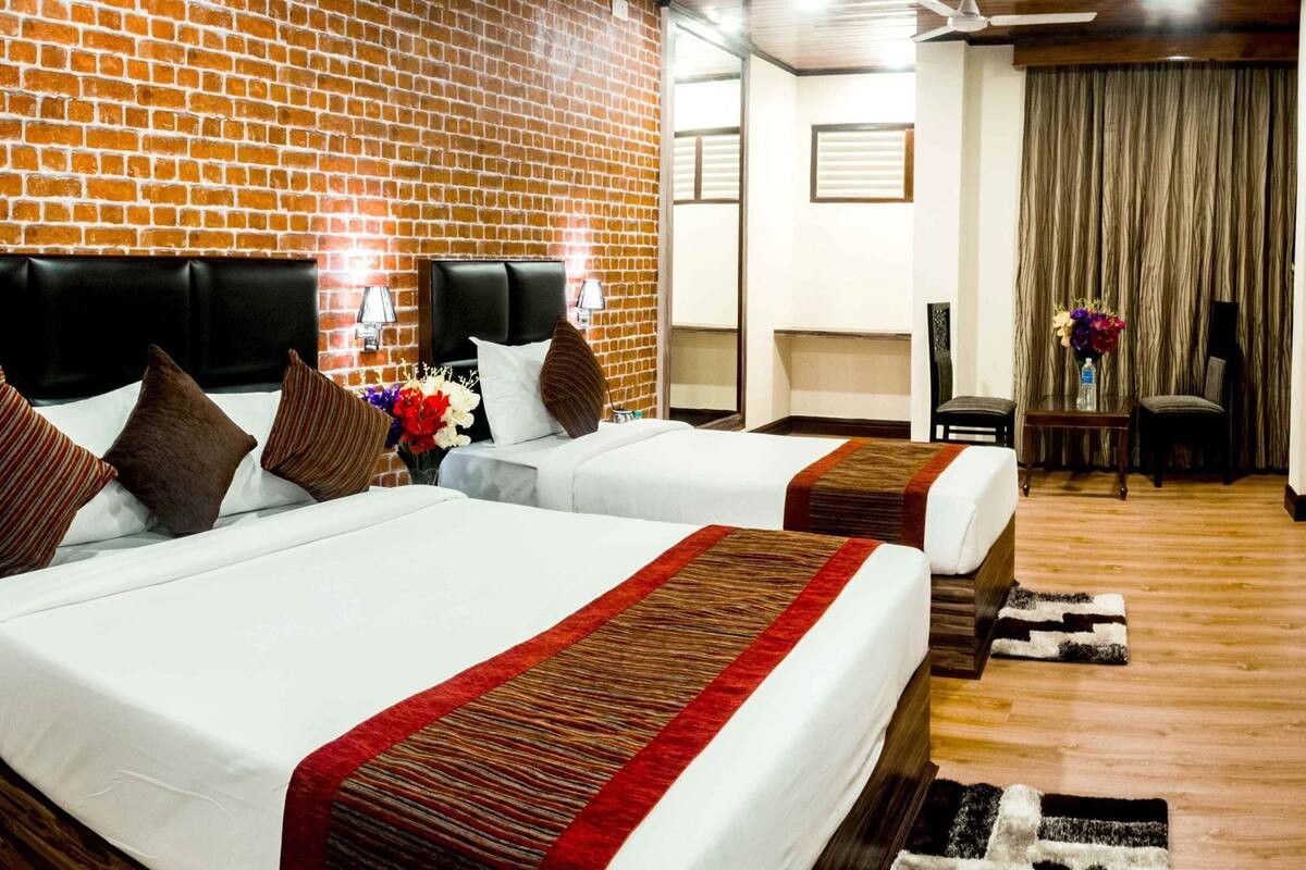 Een hotelkamer met twee bedden, een bakstenen muur, een plafondventilator en uitzicht op het omliggende landschap.