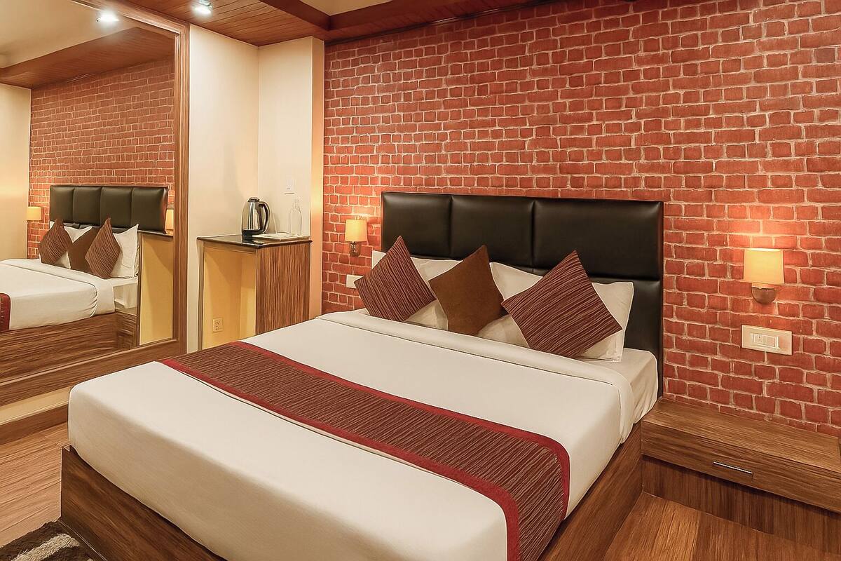 Een hotelkamer met een wand met baksteenmotief, een groot bed met hoofdbord, twee nachtkastjes met lampen en een spiegel aan de muur.