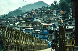 Un puente con estructura de celosía que conduce a un asentamiento en la ladera de una colina, con edificios de varios pisos.