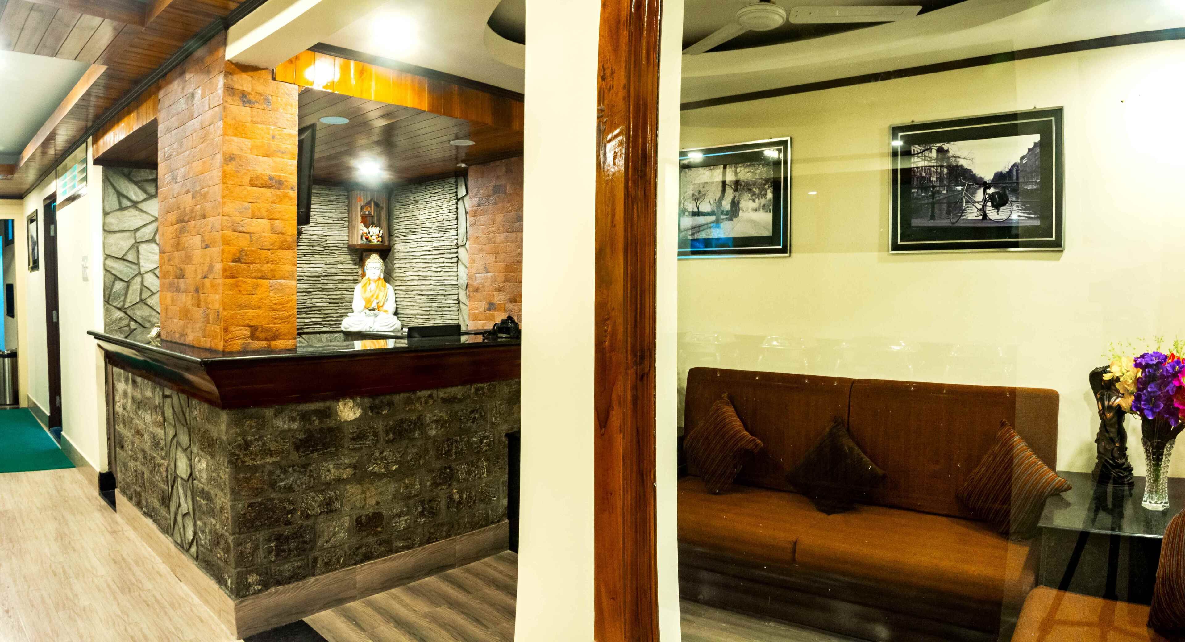 A reception area with a stone counter and a wooden reception desk. There is a sofa with cushions and a vase with flowers on a table.