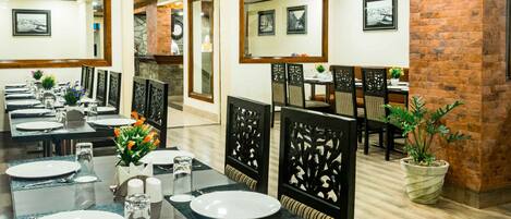 A restaurant with multiple dining tables, chairs, and potted plants.