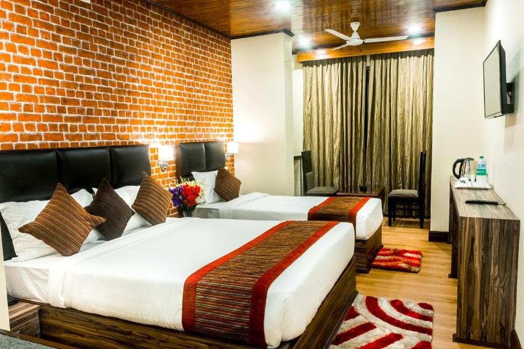 A hotel room with two beds, a brick wall, a ceiling fan, and a view of the outdoors.