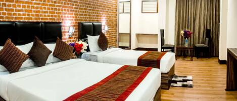 A hotel room with two beds, a brick wall, a ceiling fan, a desk with a chair, and a window with curtains.