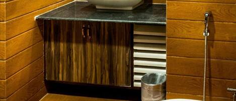 A bathroom with a wooden vanity, a sink, a mirror, a toilet, and a hairdryer mounted on the wall.