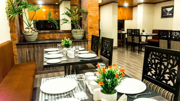 Un restaurante con decoración de madera, mesas dispuestas con platos blancos, vasos y plantas en macetas.