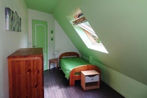 Un petit appartement d’une seule pièce, avec un plafond en pente, un puits de lumière, un lit, un bureau en bois et une petite table de chevet.